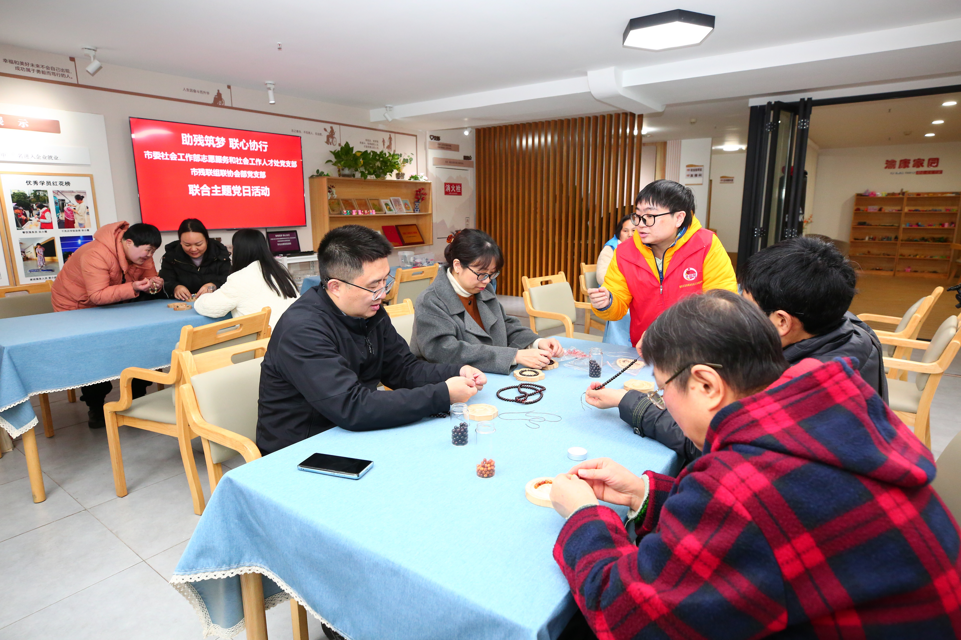 图为助残志愿者协助残疾人开展串珠手工制作